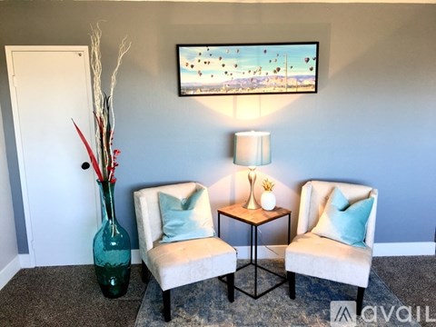 A living room with two chairs, a table, and a painting on the wall.