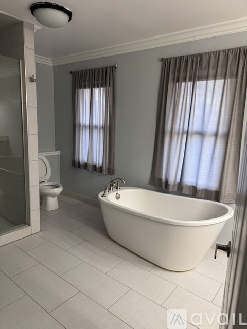 A white bathtub is in a bathroom with a toilet and a shower.