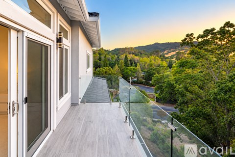 A balcony with glass railings overlooks a parking lot and trees.