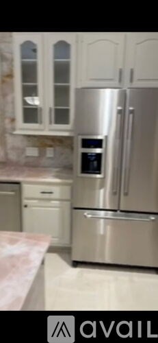A kitchen with a stainless steel refrigerator and white cabinets.