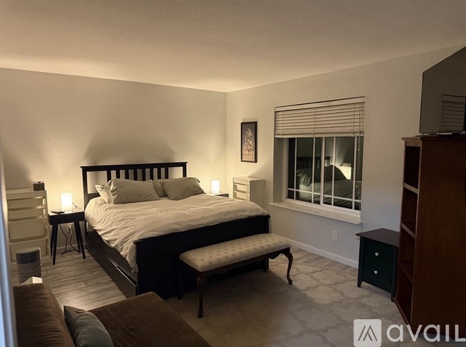 A bedroom with a large bed and a window with blinds.