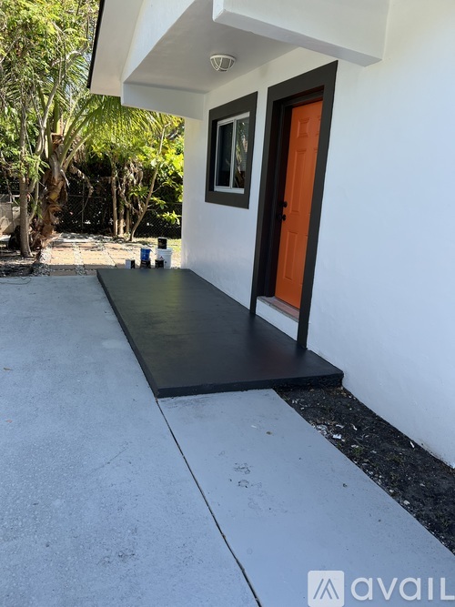 A white house with a black door and a brown mat on the ground.