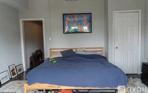 A bedroom with a bed, a painting on the wall, and a door.