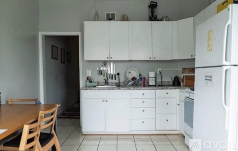 A kitchen with white cabinets and appliances, a wooden table and chairs, and a tiled floor.
