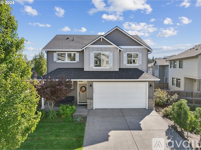 A two-story house with a garage is surrounded by a well-maintained lawn and trees.