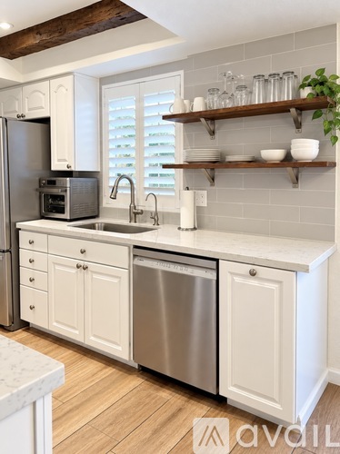 A kitchen with white cabinets and a wooden shelf above the sink.