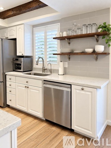 A kitchen with white cabinets and a wooden shelf above the sink.