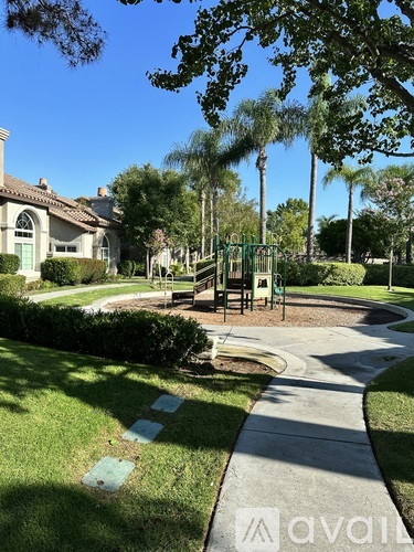 A walkway in a park with a playground and houses in the background.