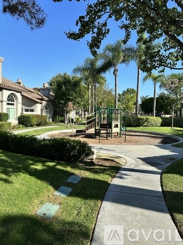 A walkway in a park with a playground and houses in the background.