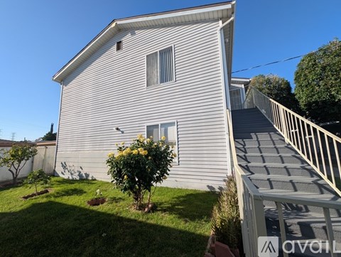 A house with a white siding exterior and a small tree with yellow flowers in front of it.