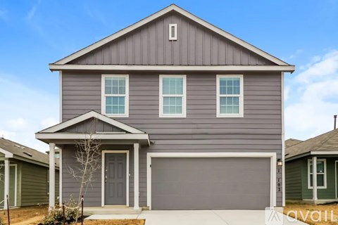 A grey house with a garage door and a tree in front.