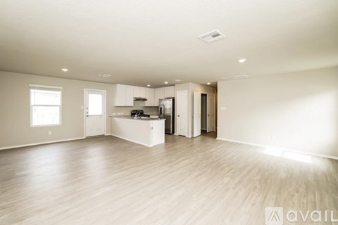 A spacious room with wooden flooring and a kitchen area in the background.