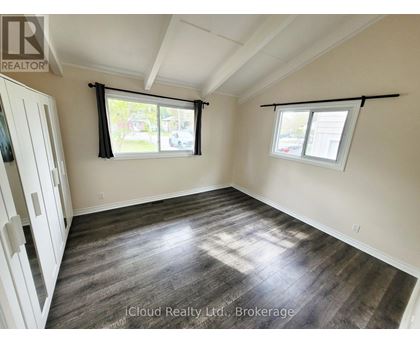 A room with wooden flooring and two windows with black frames.
