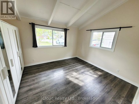 A room with wooden flooring and two windows with black frames.