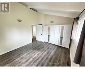 A room with wood flooring and white walls, with a window on the right side.