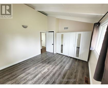 A room with wood flooring and white walls, with a window on the right side.