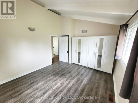 A room with wood flooring and white walls, with a window on the right side.