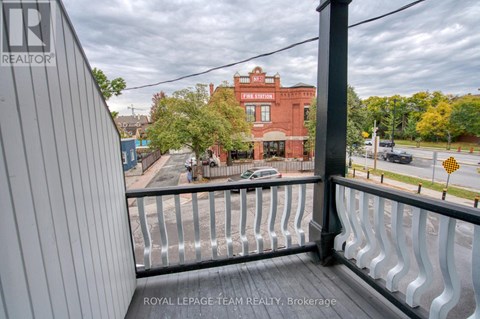 A balcony with a metal railing overlooks a street with cars and buildings.