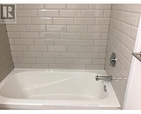 A white bathtub in a bathroom with white tiles.