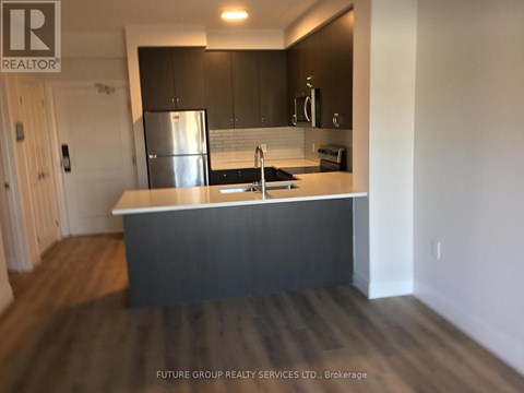 A kitchen with a stainless steel refrigerator and dark wood flooring.