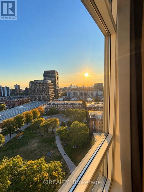 A sunset view from a window overlooking a cityscape with trees in the foreground.
