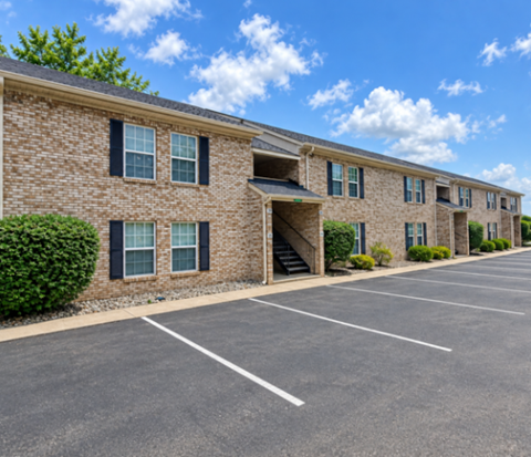 A row of brick apartment buildings with a parking lot in front.