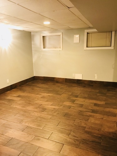 A room with wooden flooring and two windows.