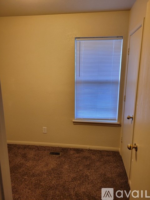 A room with a carpeted floor, a window with blinds, and a door.