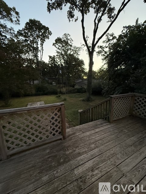 A wooden deck with lattice work and a bench overlooks a grassy area.