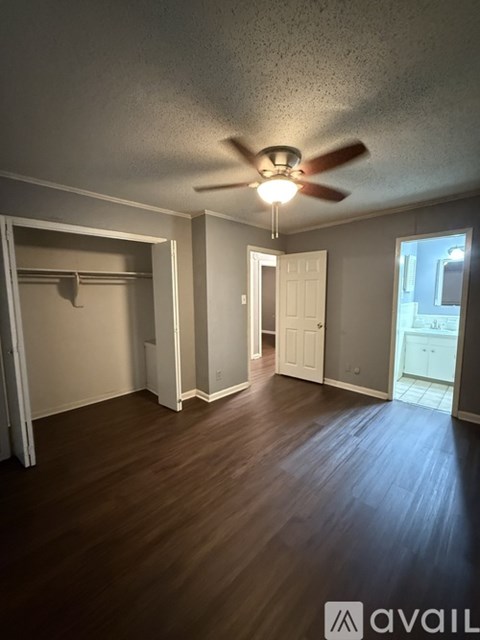 A room with a ceiling fan and light, wooden floors, and a doorway leading to another room.