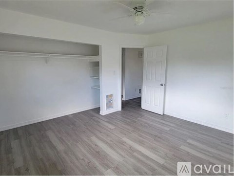 A room with a ceiling fan and light, a door, and a wall with a small white square on it.