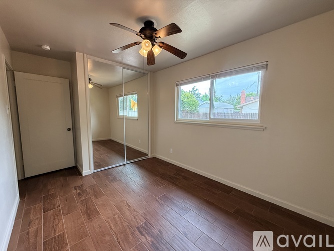 A room with a ceiling fan and a window with a view of a house and trees outside.