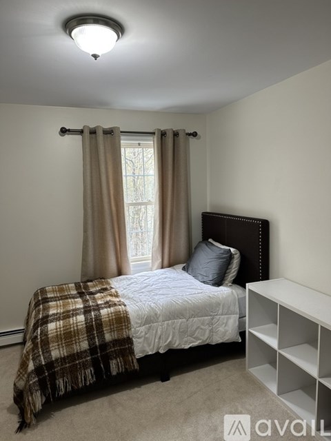 A bedroom with a bed, a window with curtains, and a nightstand with a lamp.