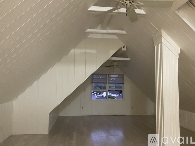 A spacious attic room with a window and a fan.