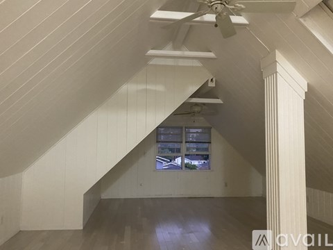 A spacious attic room with a window and a fan.