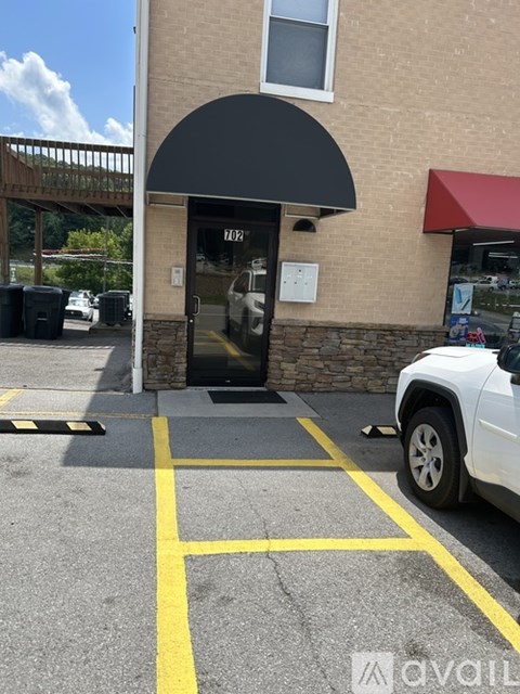 A white car is parked in a parking lot in front of a building with a black awning.