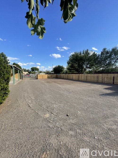 A gravel driveway leads to a wooden fence and a building.