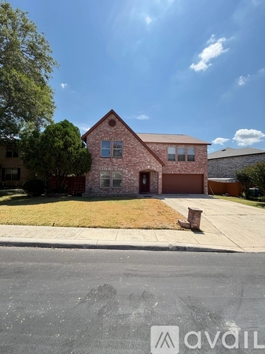 A house with a brick facade and a brown garage door is situated on a street with a sidewalk and a tree.