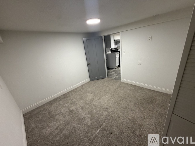 A room with a grey carpet and a white wall with a door on the left side.