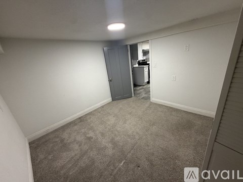 A room with a grey carpet and a white wall with a door on the left side.