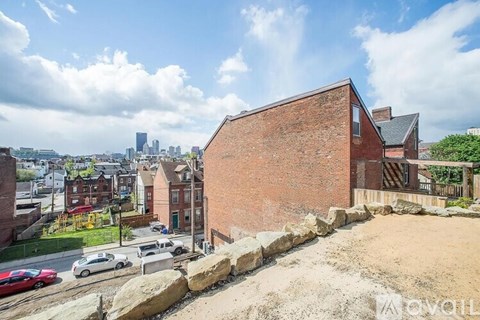 A red brick building with a green roof is in the foreground with a city skyline in the background.