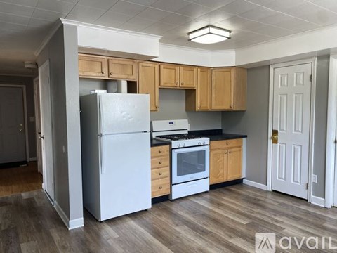 A kitchen with a white refrigerator, wooden cabinets, and a white door.