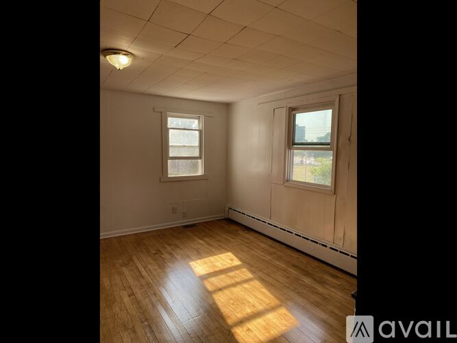 A room with wooden flooring and two windows.