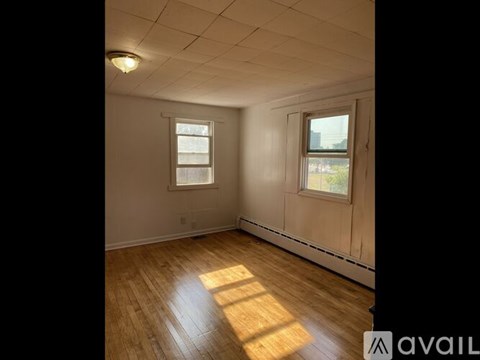 A room with wooden flooring and two windows.