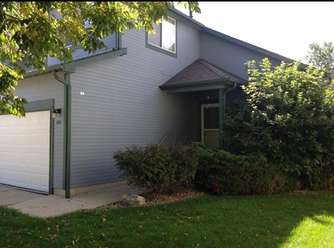 A house with a grey garage door and a green bush.