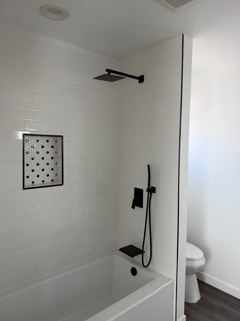 A white tiled bathroom with a shower and toilet.