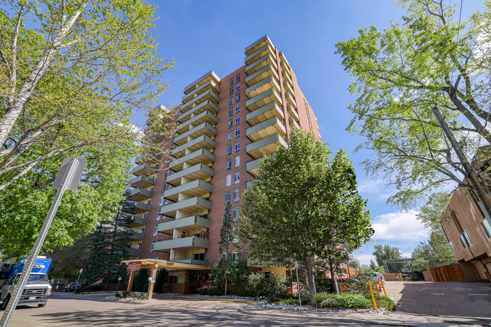 A tall apartment building with a parking lot in front.