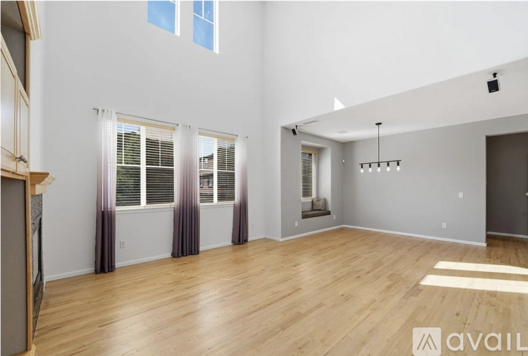 A spacious room with wooden floors and a large window with curtains.