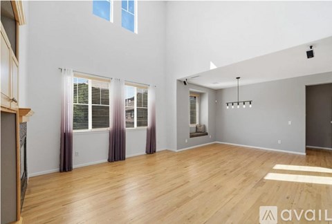 A spacious room with wooden floors and a large window with curtains.