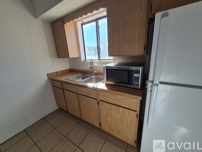 A kitchen with a white fridge, wooden cabinets, and a window.